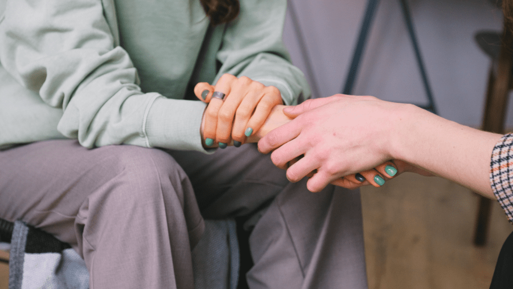 Two people, sitting across from one another in an office, holding hands.